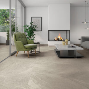 Sala moderna con suelo porcelánico beige imitación piedra, chimenea, sofá gris y butaca verde.