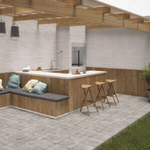 Terraza con suelo de azulejo gris, barra y banco en madera, cojines y planta