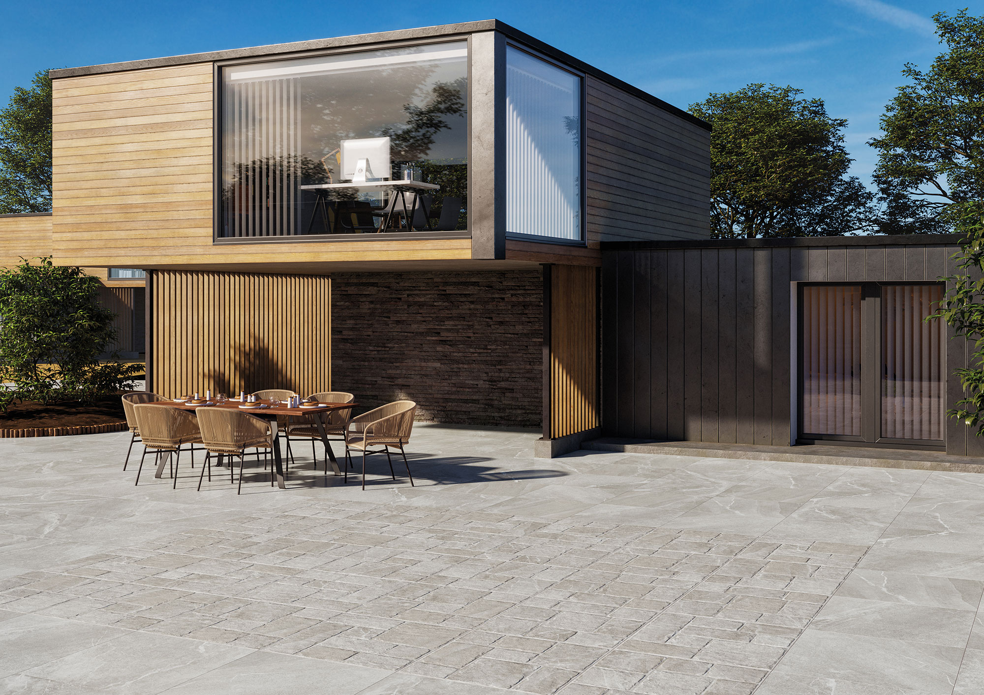 Patio con pavimento cerámico gris, adoquinado central y muebles exteriores frente a vivienda moderna