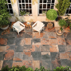 Patio con pavimento cerámico de losas multicolor, dos sillones blancos y abundante vegetación