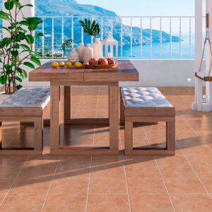 Terraza con pavimento cerámico terracota, mesa de madera, bancos acolchados y vistas al mar