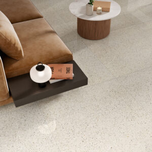 Salón con sofá marrón sobre pavimento cerámico jaspeado beige, mesa redonda y lámpara.