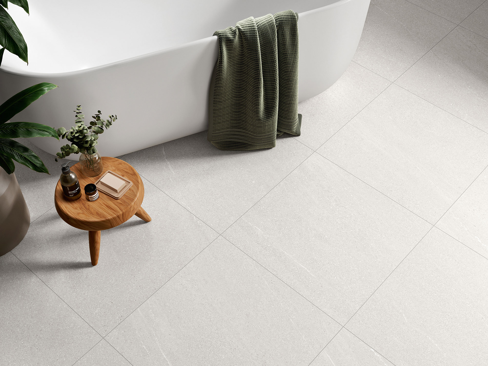 AMB-HALTON-WHITE-60X60-DETALLE Baño con bañera blanca sobre pavimento cerámico gris claro, mesa de madera y toalla verde.