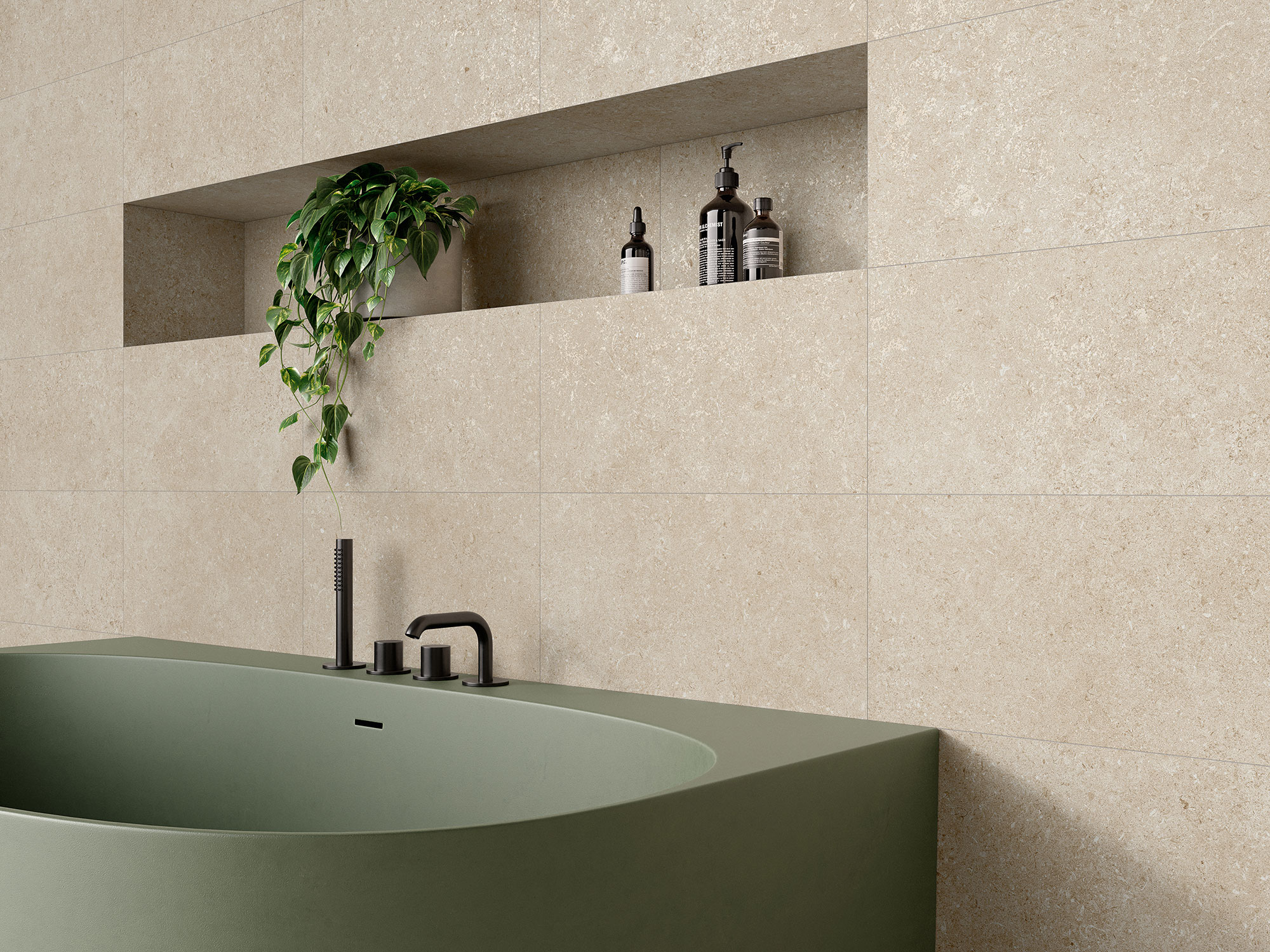 Bañera verde frente a azulejos beige tipo piedra, nicho con planta y accesorios