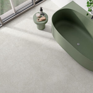 Baño con bañera verde y pavimento cerámico beige junto a ventanal.