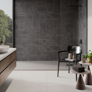 Baño expositivo con muro de azulejos geométricos oscuros, lavabo y silla