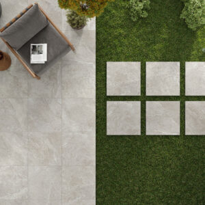 Terraza con pavimento cerámico gris, losetas cuadradas sobre césped, butaca y plantas