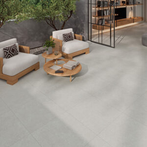 Sala de exposición con suelos cerámicos gris claro, butacas de madera y mesa baja