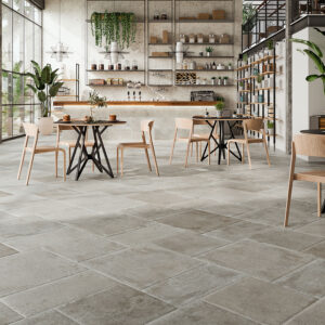 SAINT-ANDREWS-GREY-MULTIFORMATO-(1) Tienda azulejos con pavimento cerámico gris, mesas y sillas madera junto a grandes ventanales