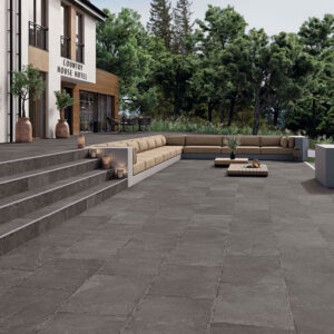 Terraza con grandes losas cerámicas gris oscuro, escalones a juego y sofá modular beige.