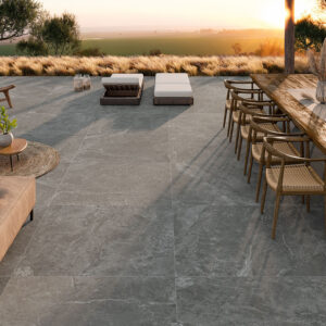 Terraza con pavimento cerámico gris efecto piedra, mesa de madera y tumbonas al atardecer