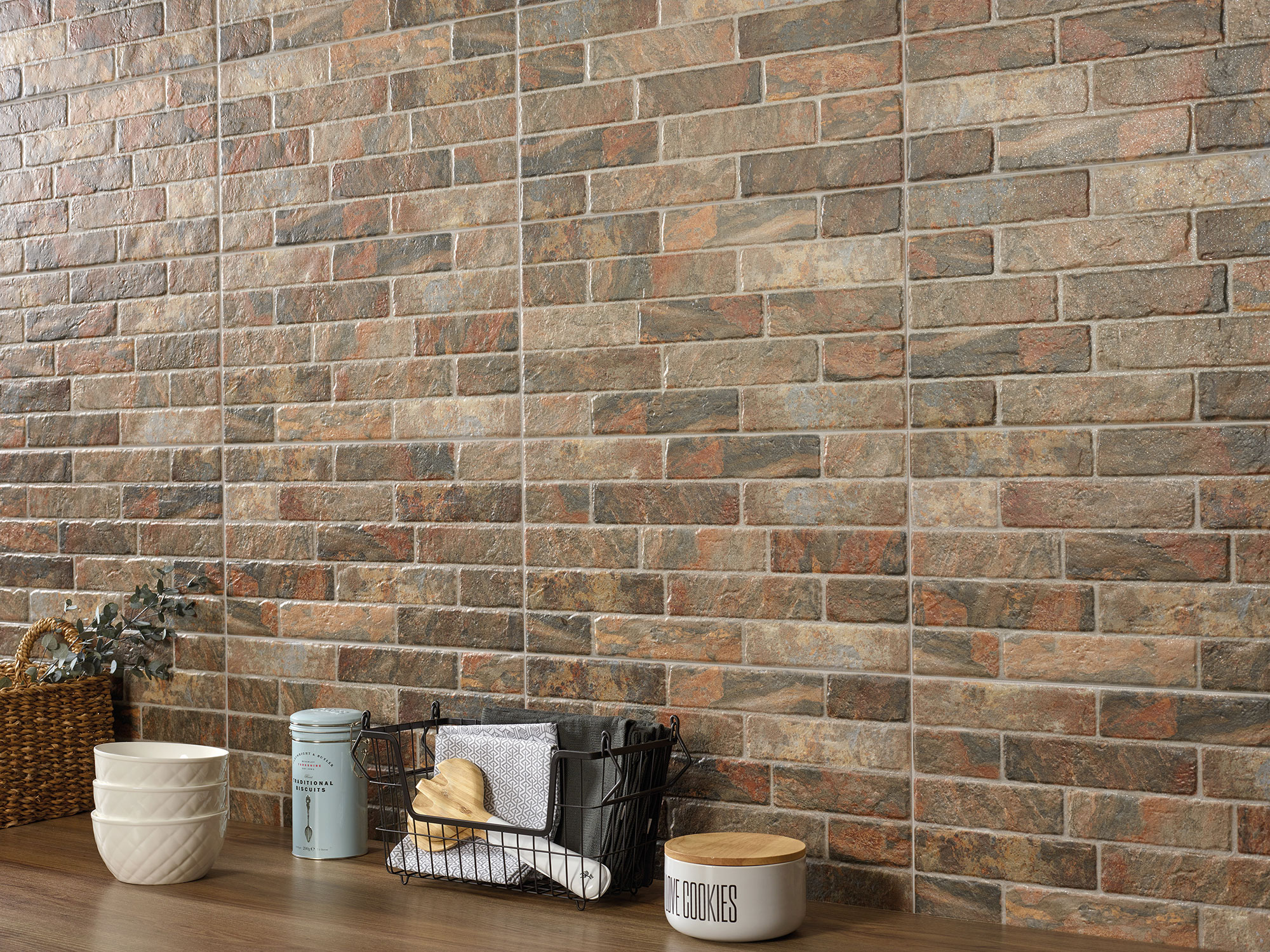 Pared de azulejos cerámicos efecto ladrillo en tonos tierra junto a encimera con utensilios.